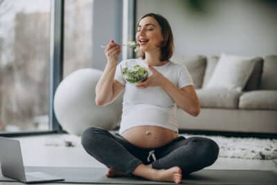 jovem mulher gravida comendo salada em casa